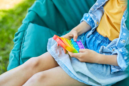 A little girl the on hanging chair outdoors play pop it, kid hands playing playing bubbles of a rainbow destressing toy, fidget toy in backyard of house on a sunny summer day, summer time vacation.の写真素材