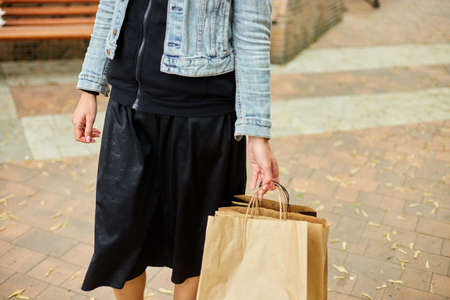 Incognito woman holding several paper bags with purchased things walking outdoors in the park, girl after shopping.の写真素材
