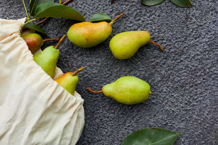Fresh ripe fruits pears in string reusable shopping eco bag on a dark background, grocery concept, Flat lay, Eco friendly, autumn harvest. Copy space.の写真素材