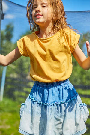 A young girl jumping up and down on her trampoline outdoors, in the backyard of the house on a sunny summer day, summertime vacation.の写真素材
