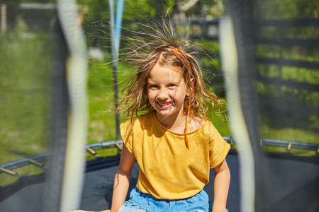Portrait of young girl with electrified hair on trampoline outdoors, in the backyard of the house on a sunny summer day, summertime vacation, Happy little child jumping on trampolineの写真素材