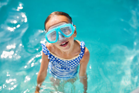 A child in goggles on the steps climbing out of the pool, little girl having fun in the swimming pool, summer vacation at home, tropical holiday resort.の写真素材