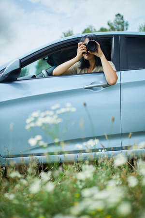 Woman photographer sitting in the car and photographing a flower field landscape, travel female take photo, space for text.の写真素材