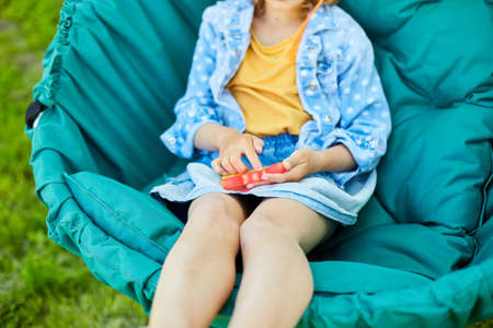 A little girl the on hanging chair outdoors play bubble fidget, fidget toy in the backyard of the house on a sunny summer day, summer time vacation.の写真素材