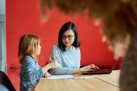 Mother working in her home office on a laptop, her daughter sits next to her and drawの写真素材