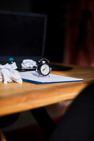 Modern workplace, wooden office desk in hardlight, sunligt with clock, sheet of paper, laptop,...