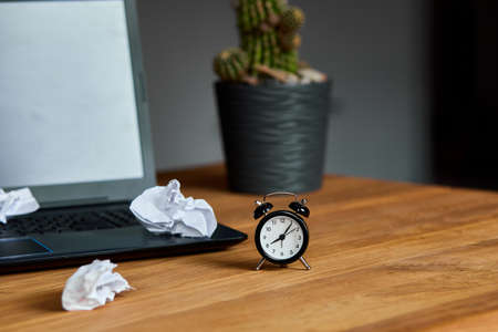 Workplace,  wooden office desk with clock, sheet of paper, laptop, notebook, crumpled paper balls...