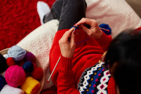 Mature female sitting in comfortable sofa and knitting while enjoying weekend at home, Senior woman knitting, relax at home do favorite hobby activity on weekend, wellbeing conceptの写真素材