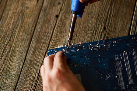 Technician or engineer is focused on repairing electronic circuit board with soldering iron.  Man...