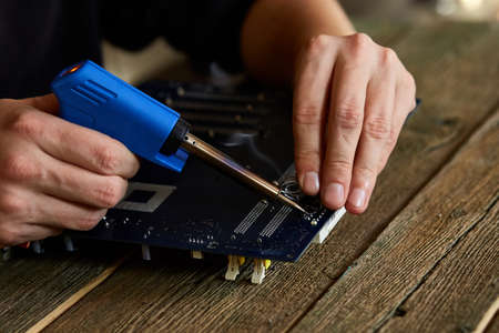 Engineer or technician repair electronic circuit board with soldering iron. Man hands soldiers computer circuit board using soldering iron. Copy space.の写真素材
