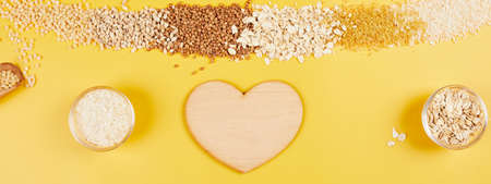 Banner of Flat lay of set of heap various grains and cereals bulgur, rice, oatmeal, buckwheat, couscous wheat seeds on yellow background with heart, copy space, space for text, top view.の写真素材