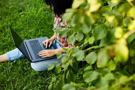 Woman freelancer in casual clothes with her computer laptop sitting on the grass at the parkの写真素材