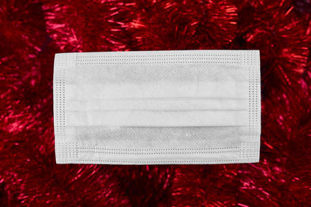 Flat lay festive christmas decoration and face medical protection mask on red tinsel backgroundの写真素材