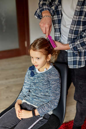 Father combing, brushing his daughter's hair at home, father and daughter smiling, family moments,...