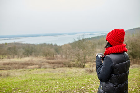 Woman in red hat and scarf, drinking tea from metal cup outdoor, Travel concept, Autumn background landscape.の写真素材