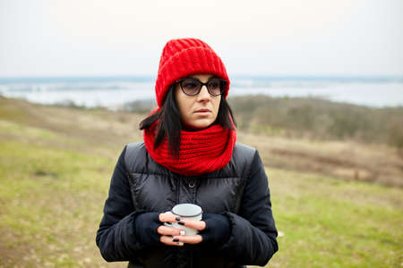 Woman in red hat and scarf, drinking tea from metal cup outdoor, Travel concept, Autumn background landscape.の写真素材