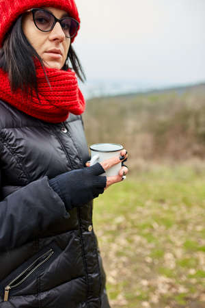Woman in red hat and scarf, drinking tea from metal cup outdoor, Travel concept, Autumn background landscape.の写真素材