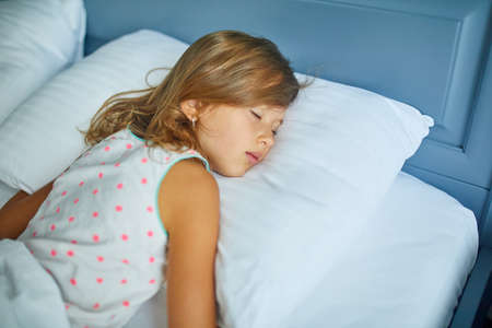 Little girl sleeping on a big and cozy bed white linen in the afternoon at home, family lifestyle,...