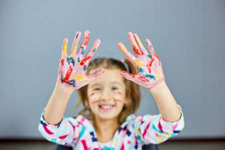 Little girl with painted colorful watercolor hands up, child sitting at the table and drawing, Art school concept, girl kid painting at homeの写真素材