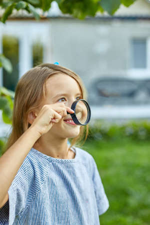 Little girl playing with a magnifying glass in her backyard at home make faces. Childhood lifestyle concept, Education, school conceptの写真素材