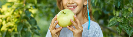 Banner Cute little girl eat green apple in home garden outdoor, happy child, make faces, autumn harvest, apple tree, Healthy nutrition diet vegetarian food lifestyle.の写真素材