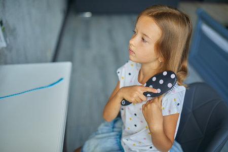 Pretty Little girl combing by herself hair in front of a mirror, brushing her hair at home, child smiling, morning routineの写真素材