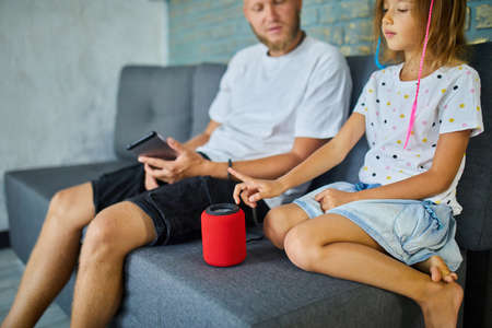 Father and daughter testing talking smart wireless speaker, controlling home devices with a voice commands, sitting on sofa at home, Concept of smart homeの写真素材