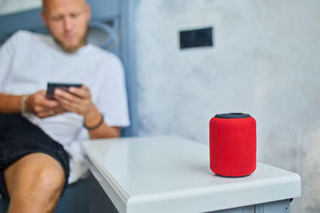 Male testing talking smart wireless speaker, man controlling home devices with a voice commands,...