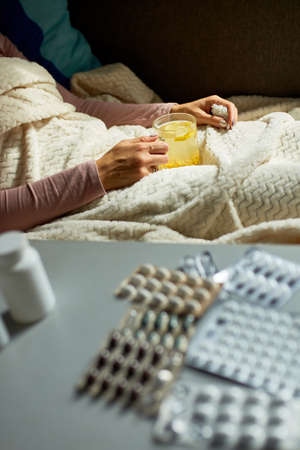 Sick woman holding mug of warm sea buckthorn tea and sitting under blanket at home, Ill lady.