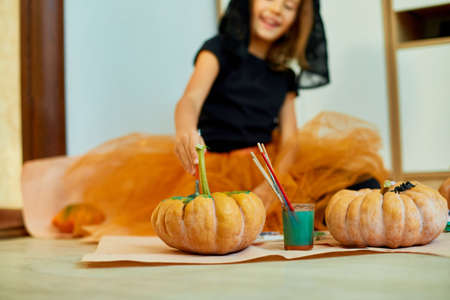 Little girl drawing face on orange Halloween Jack-O-Lantern pumpkin, Happy child decorating a pumpkin at home. Holiday decoration conceptの写真素材