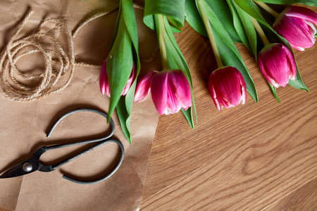 Floristic workplace with craft paper, twine Arranging pink tulips bouquet on wooden table, hobby, diy, spring gift concept, From above.の写真素材