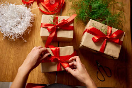 Hands of cropped unrecognisable woman packing Christmas present, Eco friendly packaging kraft paper...