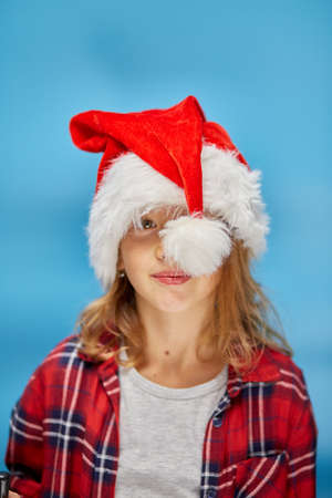 Portrait of Christmas little Girl in Santa Hat, joyful, smiling child on isolated blue studio background, place for text, Wow faceの写真素材