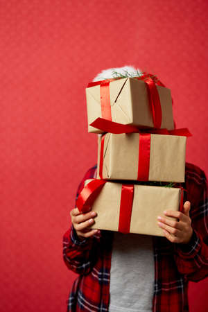Funny little girl in santa hat with many Christmas gift boxes isolated on red background, Christmas presents shopping sale, happy New Yearの写真素材