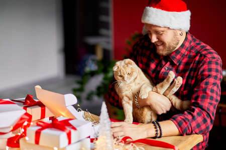 Vet Man in Santa hat and cat in hand making greeting card for New Year and Christmas, congratulation for clients or friends or family , packing presents or gifts, mail manager concept.の写真素材