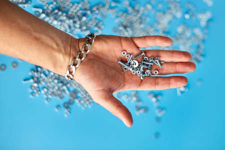Male hold in hand runs hand Metal screw, nuts and bolts on blue background, Working tools, Fixing elementsの写真素材
