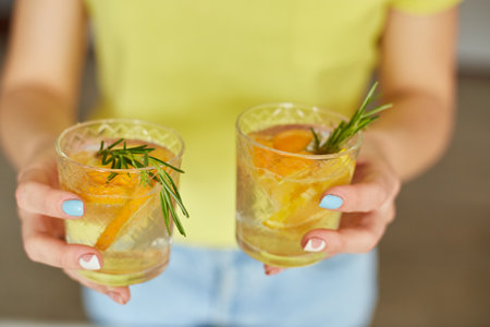 Female woman hand hold two glasses of citrus orange and rosemary fresh lemonadeの写真素材