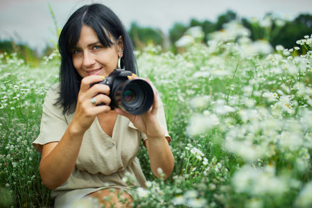Portrait of Female photographer take photo outdoors on flower field landscape holding a camera, woman hold digital camera in her hands. Travel nature photography, space for text, top view.の写真素材