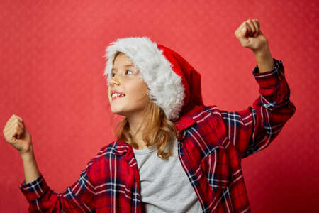 Christmas little Girl in Santa Hat, smiling and dancing, happy child on isolated red studio background, Merry Christmasの写真素材