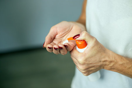 Mature woman holding bottle cream and applying moisturizing hand cream at home, Concept of health...