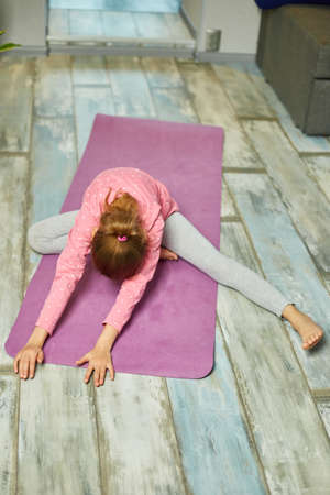 Little girl doing stretching exercises, practicing yoga on fitness mat at home, Playing sports, Healthy lifestyle. Kids sport home quarantineの写真素材
