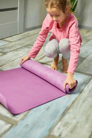 Child, little girl rolling up yoga pilates mat on floor after stretching exercises, practicing yoga, Playing sports, Healthy lifestyle.の写真素材