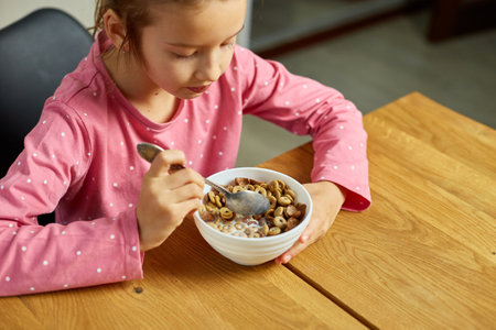 Cute little girl enjoy eating cereal with milk for morning breakfast with appetite, How tasty healthy food, Slow motion of beautiful child having breakfast at home.の写真素材