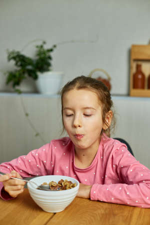 Cute little girl enjoy eating cereal with milk for morning breakfast with appetite, How tasty healthy food, Slow motion of beautiful child having breakfast at home.の写真素材