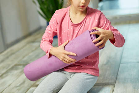 Child, little girl rolling up yoga pilates mat on floor after stretching exercises, practicing yoga, Playing sports, Healthy lifestyle.の写真素材