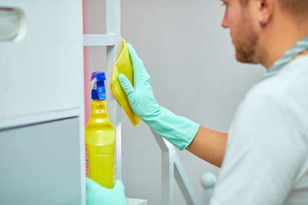 Bearded man cleaning home table surface with towel and gloves, disinfectant spray bottle, breaking gender stereotypes, gender-neutral.の写真素材
