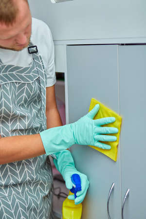 Bearded man cleaning home table surface with towel and gloves, disinfectant spray bottle, breaking gender stereotypes, gender-neutral.の写真素材