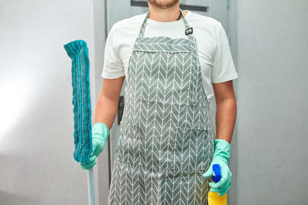 Bearded man in gloves with cleaning stuff, mop, disinfectant spray bottle in hand, breaking gender stereotypes, gender-neutral, household conceptの写真素材