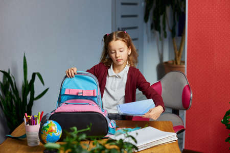 Schoolgirl put books and notes into backpack at home, pupil prepare staff for education, School...