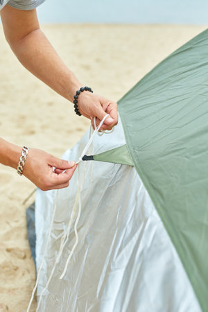 Young male tourist puts a green tent in the beach coast . The man sets up a camp on a hike, collects a tent alone, new normal travel.の写真素材